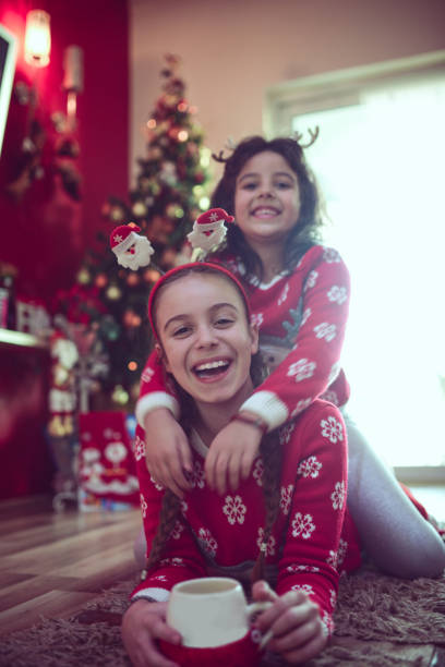 istock Two Little Sisters Hugging Under Christmas Tree and Drinking Hot Beverage 856083894