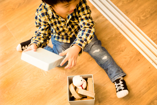 A Japanese boy is sitting on the flooring floor and playing with a toy box.