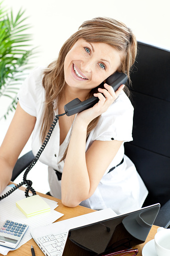 Gladsome woman sitting on a chair in her office and phoneing