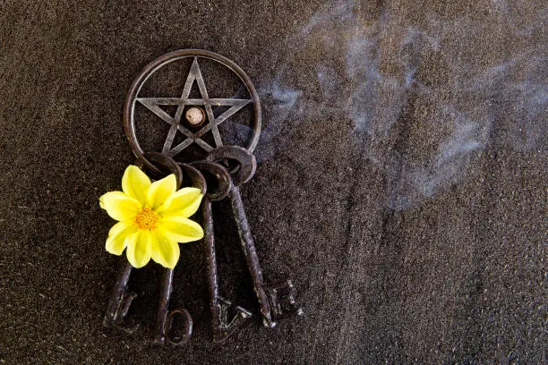 Photo of Incense burning in gray metal pentagram with love keyring on slate background with yellow dahlia flower