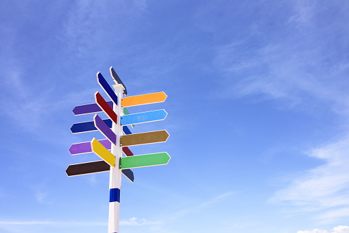 Empty wooden signpost with colorful arrows on blue sky background