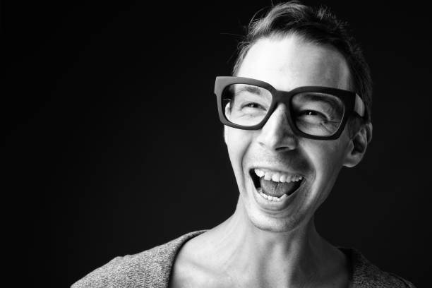 Studio shot of rebellious man wearing eyeglasses against black background in black and white horizontal shot