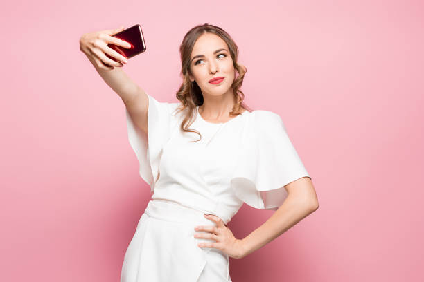 portrait of a young attractive woman making selfie photo with smartphone on a pink background - made man object imagens e fotografias de stock