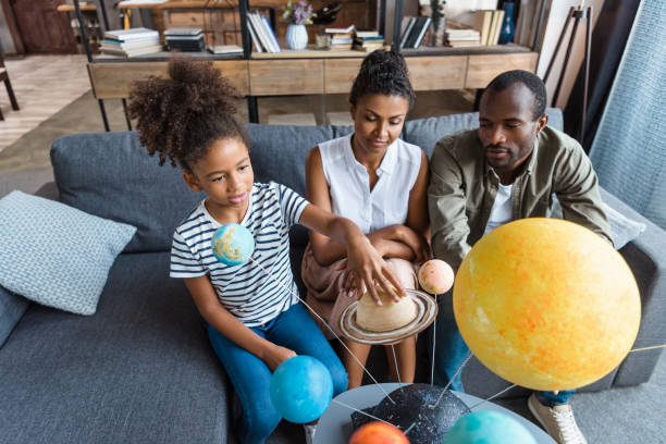 Girl and parents with solar system model Little girl and her parents sitting on a couch with a big solar system model in front of them the black womens expo stock pictures, royalty-free photos & images