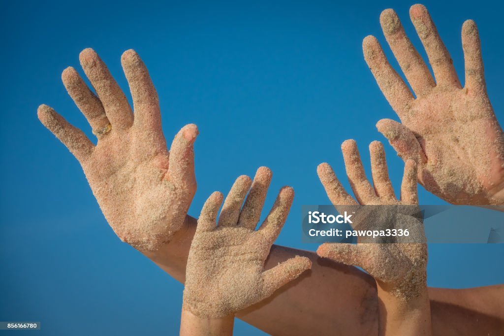 Adult and child hands covered in beach sand Close up of a  sand covered hands of mother and daughter with blue sky background Adult Stock Photo