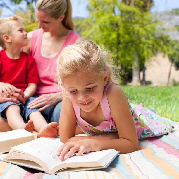 istock Concentrated blond girl reading while having a picnic with her family 856173798