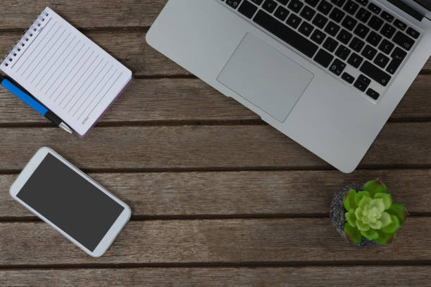 istock Laptop, pot plant, notepad, pen and mobile phone on wooden plank 856181000