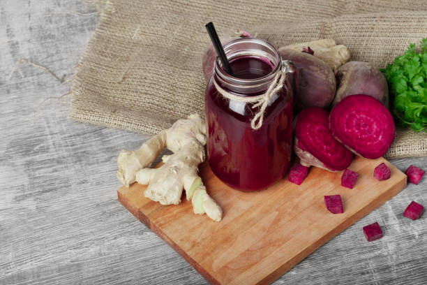 istock A mason jar of beetroot juice with black straw on a wooden background. A ginger, beets, and parsley on a cutting board. 856185020