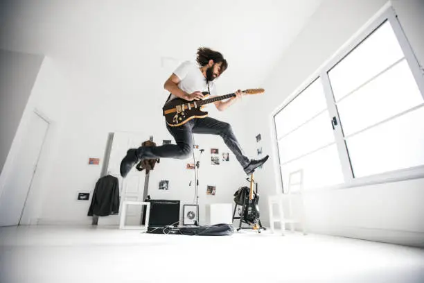 Young man jumping while playing electric guitar. Guitar head is changed, and it's not a copy of any existing guitar. Guitar head does not look like any other existing guitar head.