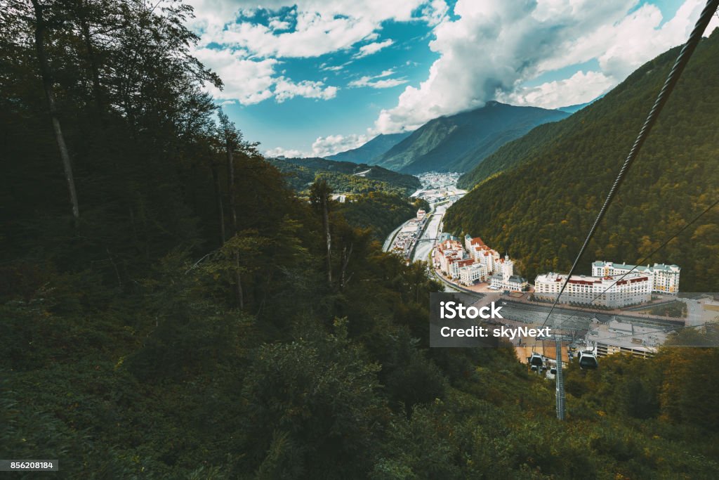 Landscape of cableroad in mountains with settlement Wide-angle shooting from funicular cabin of autumn mountain scenery with small settlement Estosadok in valley, filled with multiple resort buildings; ropeway on the right, sunny day, Sochi, Russia Architecture Stock Photo