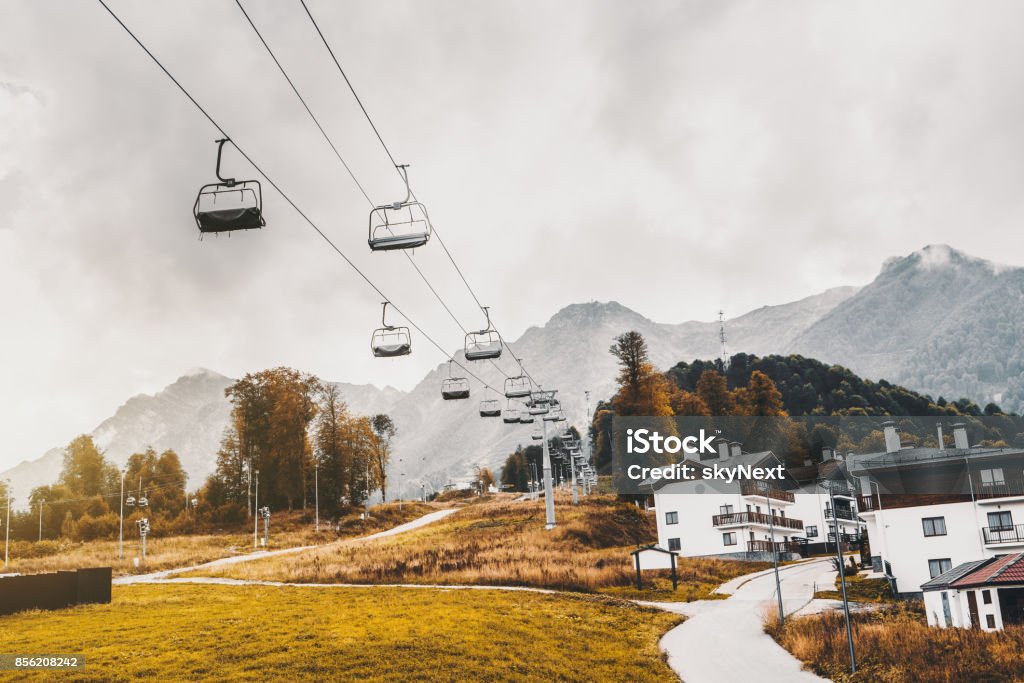Ropeway in village resort Autumn landscape: ropeway stretching into distance over hills with houses of Olympic village, trees, cell connection towers, meadows and the road; low clouds, Estosadok district, Sochi, Russia Autumn Stock Photo