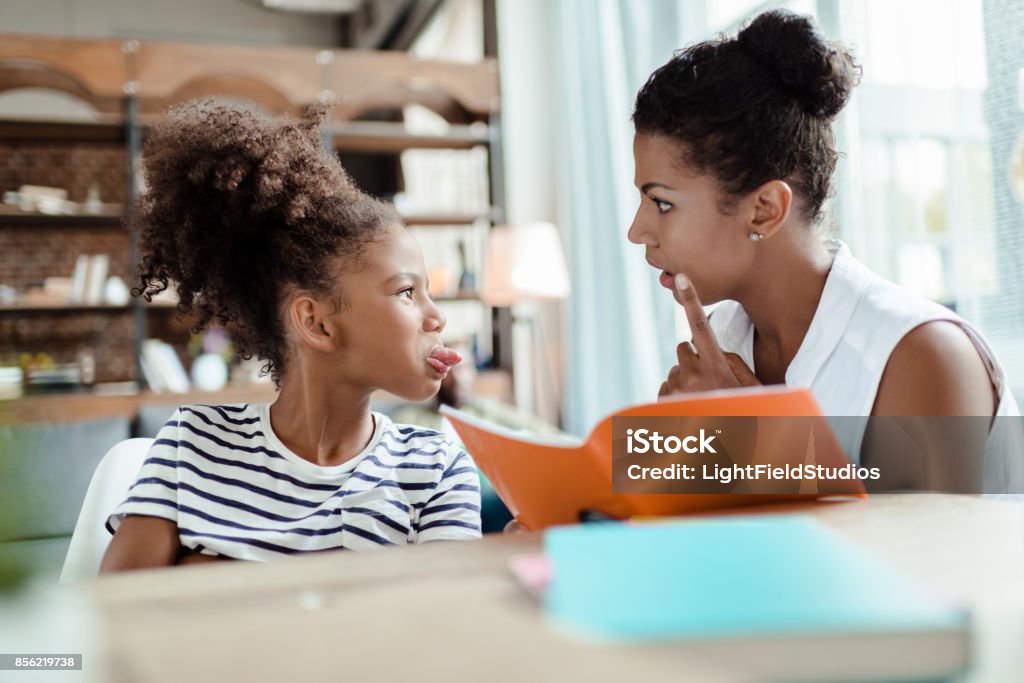 Mom scolding daughter Mom holding a notebook and scolding her daughter for sticking her tongue out Anger Stock Photo