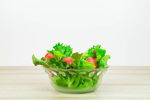 Salad vegetables in glass bowl on wooden table on white background side view, healthy lifestyle concept