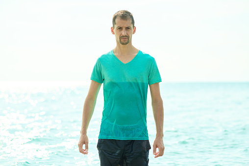 lifestyle shot of young man coming out from the sea side with his t-shirt wet, vacation time.