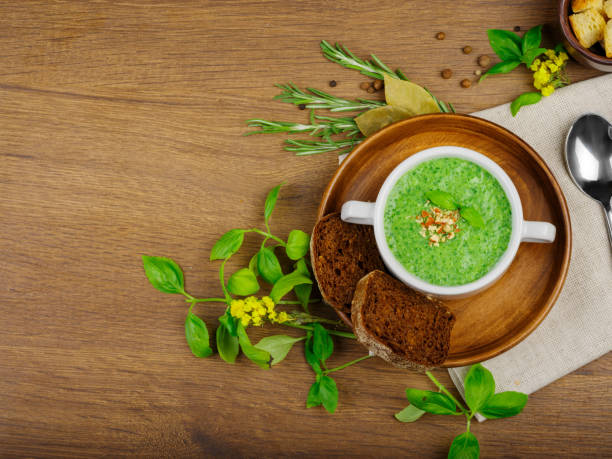 istock Green vegetable cream soup in white bowl with dark bread and celery on a wooden background. Food concept. 856273630
