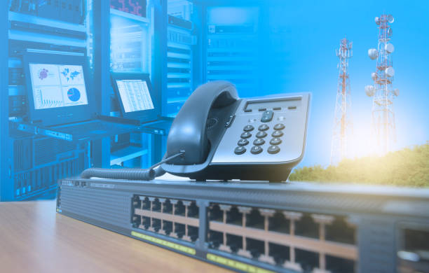 IP telephone on networking switch with blurred server rack cabinet data center room and telecommunication tower stock photo