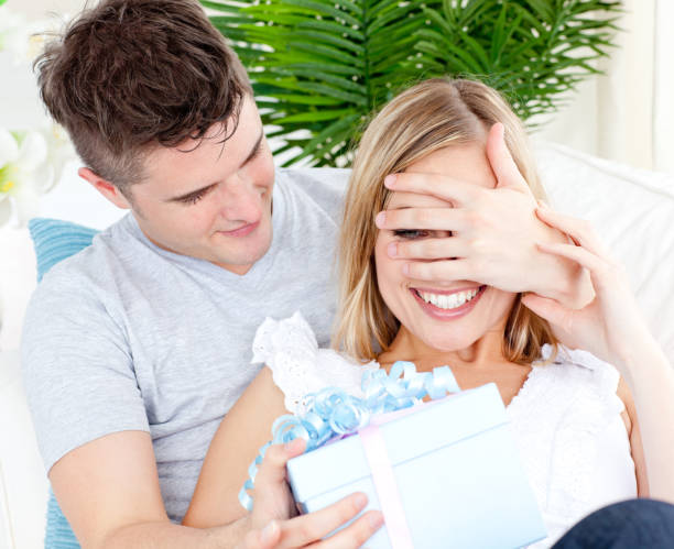 istock Young couple looking at the camera with a present in the livingroom 856295514