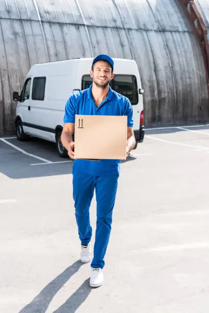 smiling delivery man carrying cardboard box