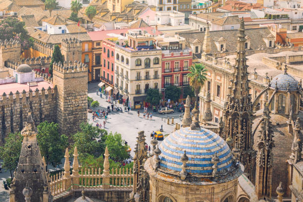 City of Seville, in the foreground the spires and domes of Seville cathedral, in the background an old town street with people moving about.