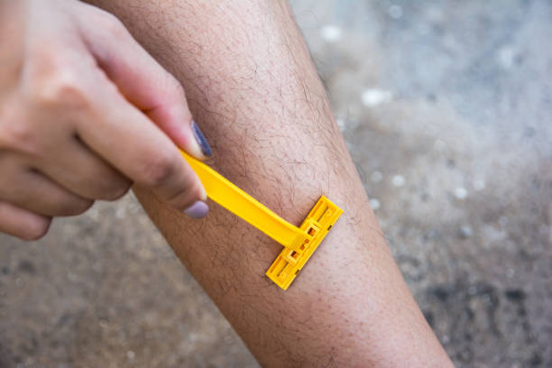 woman shaving hairy legs with plastic razor - smooth part of colors yellow imagens e fotografias de stock