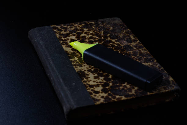 Old book lying on a black countertop and office marker. black background