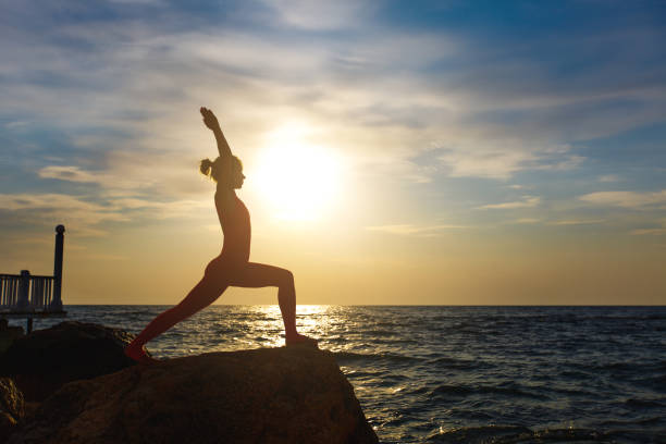 A woman in a red suit practicing yoga on stone at sunrise near the sea The woman in a red suit practicing yoga on stone at sunrise near the sea yoga stock pictures, royalty-free photos & images