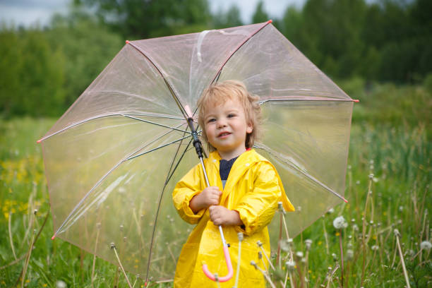 istock A little child in a yellow raincoat under an umbrella on a summer day. 856372010