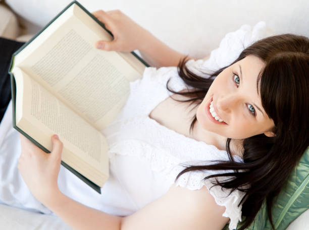 istock Bright brunette teenager holding a book smiling at the camera 856379694