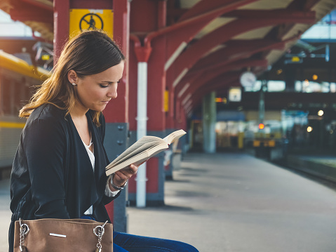 A beautiful young woman is reading while waiting for the train at the station. Shot in 4K resolution.