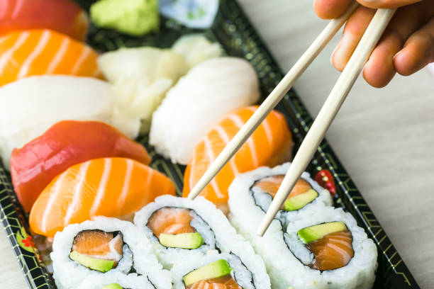 istock Hand using chopsticks pick Sushi, Sashimi and Futomaki rolls.  Fresh made Sushi set with salmon, prawns, wasabi and ginger. Traditional Japanese cuisine. 856400528