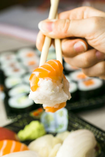 istock Hand using chopsticks pick Sushi, Sashimi and Futomaki rolls.  Fresh made Sushi set with salmon, prawns, wasabi and ginger. Traditional Japanese cuisine. 856400560