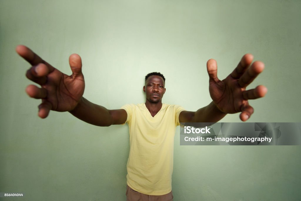 african man with his arms outstretched standing against green wall Wide angle portrait of african man with his arms outstretched standing against green wall Wide Angle Stock Photo