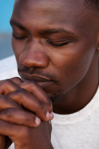 istock young african man praying with hands clasped and eyes closed 856406882