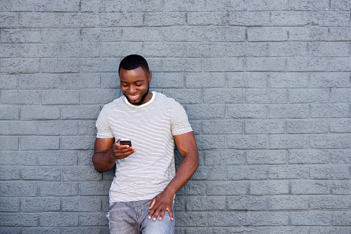 Portrait of smiling man with mobile phone leaning on brick wall