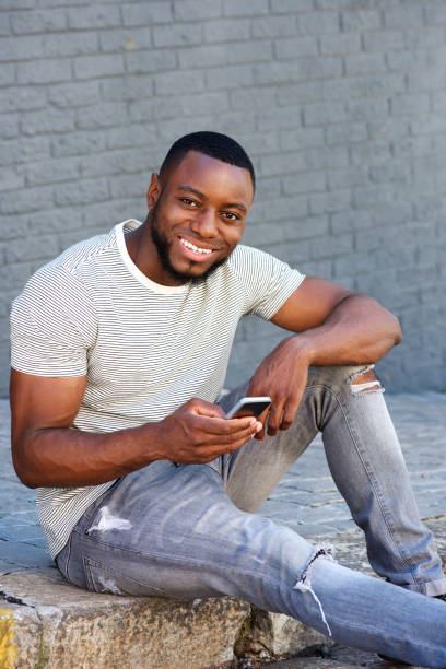 istock smiling man with smart phone sitting on curb outside 856407448