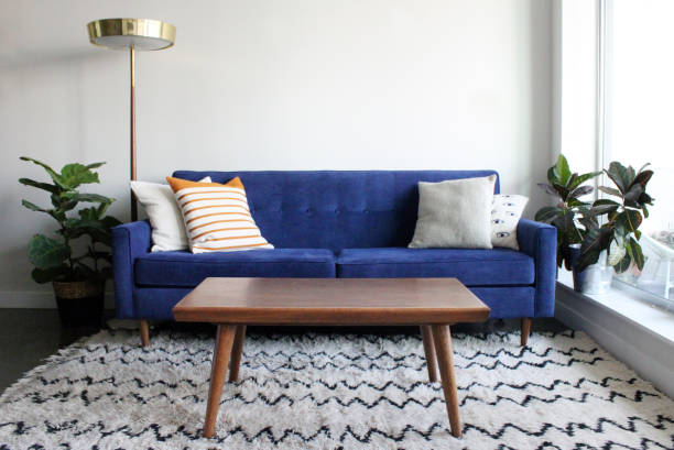 Blue Suede Mid Century Modern Couch in Minimalist Apartment Setting Low angle shot of a royal blue suede mid century modern 4 seater sofa and teak coffee table. Set in a modern apartment living room complete with mid century furnishings, moroccan rug and potted plants. coffee table stock pictures, royalty-free photos & images