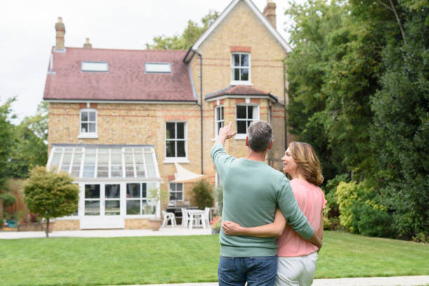 istock Mature man with arm around woman and pointing towards their house 856410946