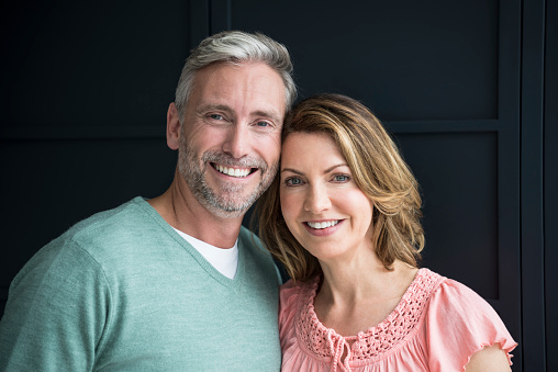 Attractive mature couple leaning close to each other with cheerful expressions, in front of dark blue background