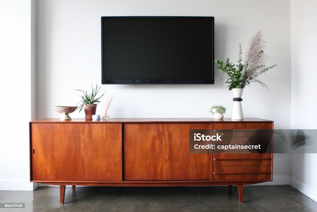 Wall mounted TV in Mid Century Modern Furnished Apartment A 50 inch flat screen TV wall is mounted above a mid century modern teak credenza. Decorated with simple, modern pottery, plants, candle and aromatherapy. Television Set Stock Photo