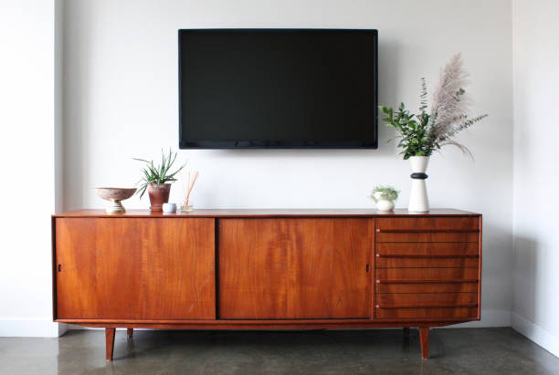 Wall mounted TV in Mid Century Modern Furnished Apartment A 50 inch flat screen TV wall is mounted above a mid century modern teak credenza. Decorated with simple, modern pottery, plants, candle and aromatherapy. sideboard photos stock pictures, royalty-free photos & images