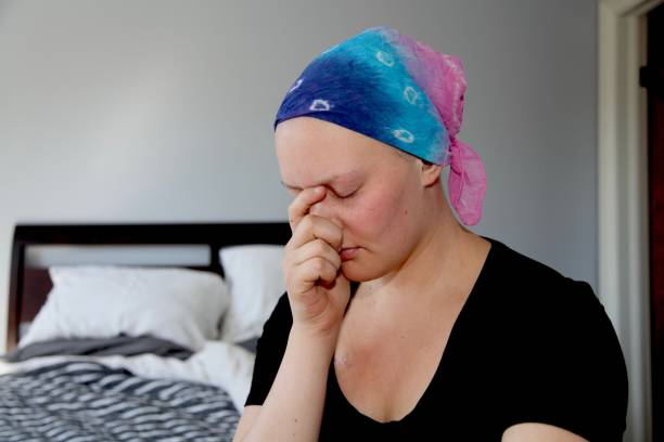 istock Young cancer patient in headscarf holds hands to face in stress and sadness 856427652