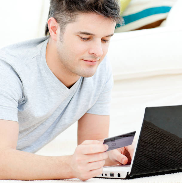 istock Positive young man holding a card using his laptop on the floor 856441162