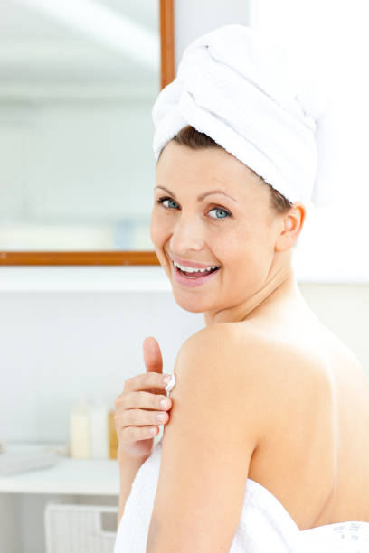 istock Delighted young woman putting cream on her body looking at the camera 856444854