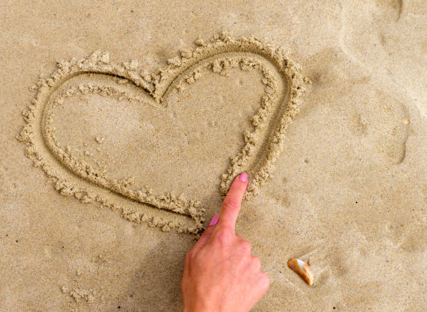 istock Woman drawing heart on sand. Cropped image, selective focus. 856455718