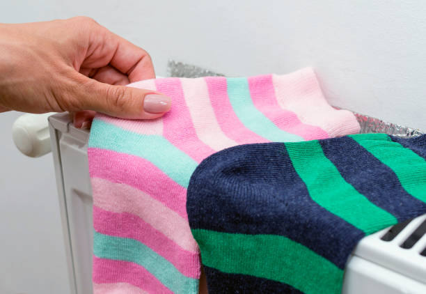istock Woman's hand hold socks that dry on radiator. Domestic heating radiator. 856458434