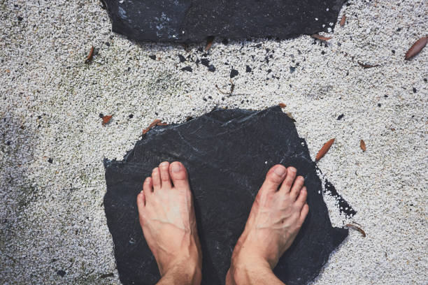 Human feet standing on black stone in white sand Human feet standing on black stone in white sand peacful stock pictures, royalty-free photos & images