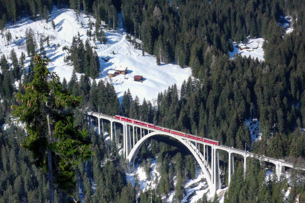 red train crossing a bridge red train crossing a bridge over a deep gorge in the forest in Switzerland in the Alps in winter near Arosa arosa stock pictures, royalty-free photos & images