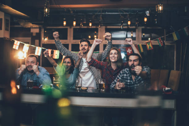 Celebrating in the pub Group of young people, sitting in a pub all together, watching a sports game. fan enthusiast photos stock pictures, royalty-free photos & images
