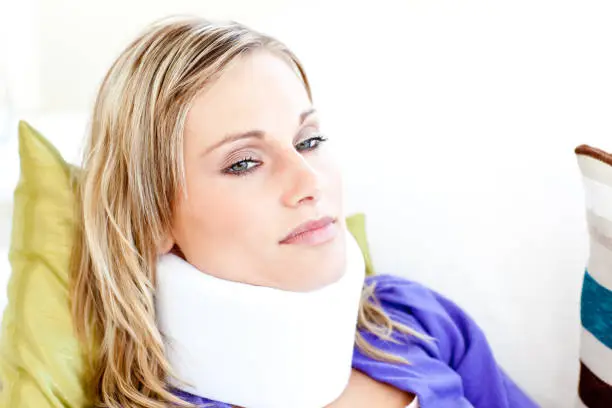 Beautiful woman wearing neckbrace lying on a sofa against a white background