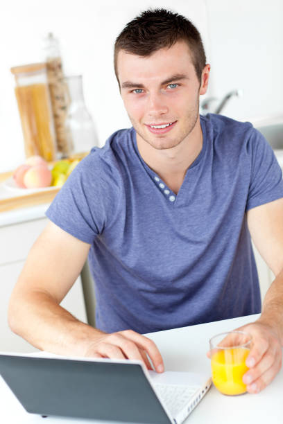 istock Charming young man using his laptop holding orange juice in the kitchen 856496770